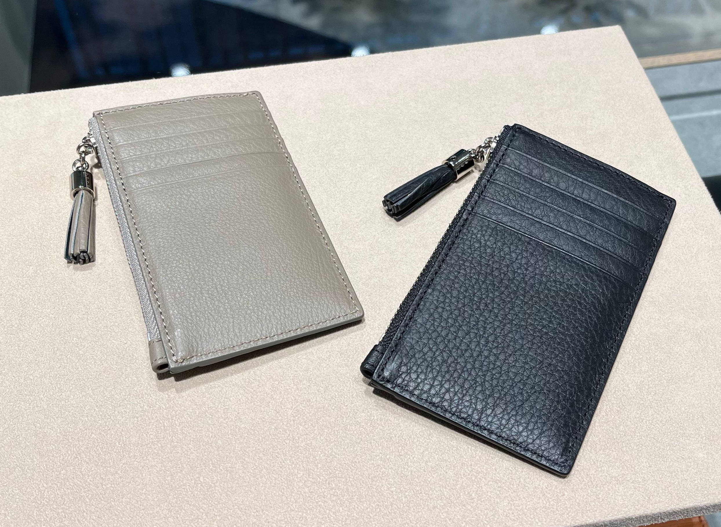 Two wallets, one beige and one black, displayed on a light-colored surface.
