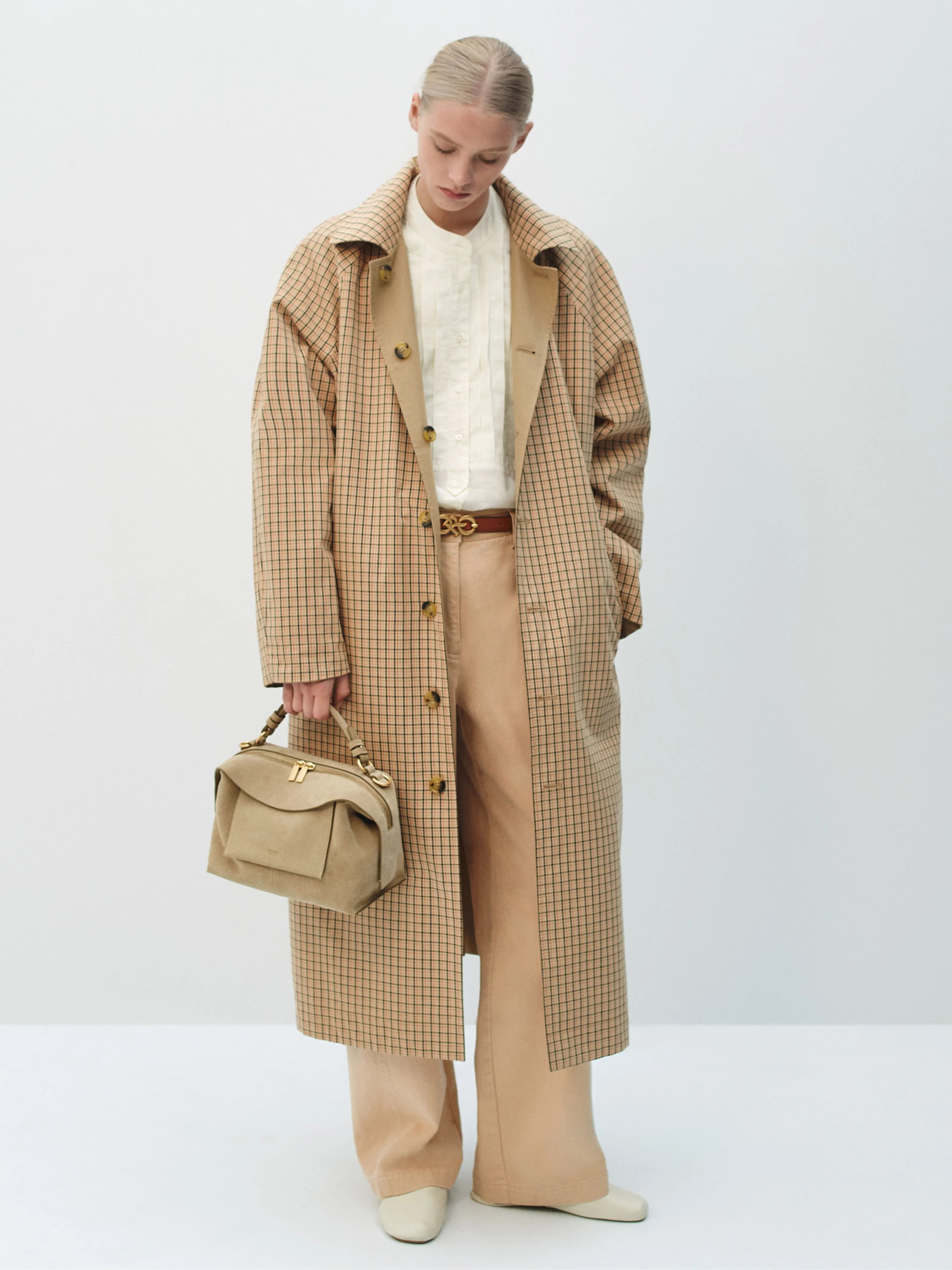 Person in a checked coat and beige trousers holding a handbag.