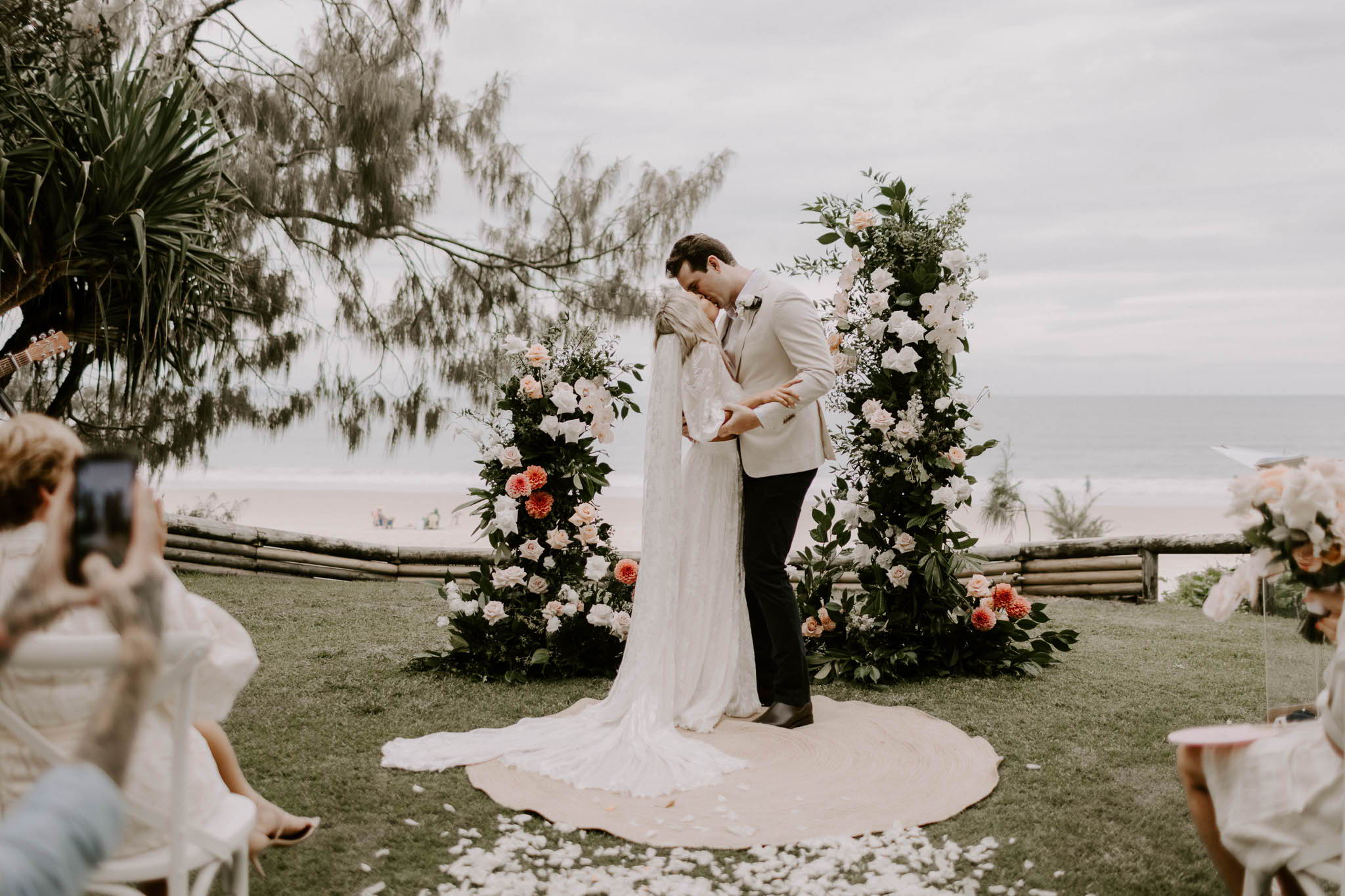 Bride and groom kissing at altar on grass  overlooking Laguna Bay