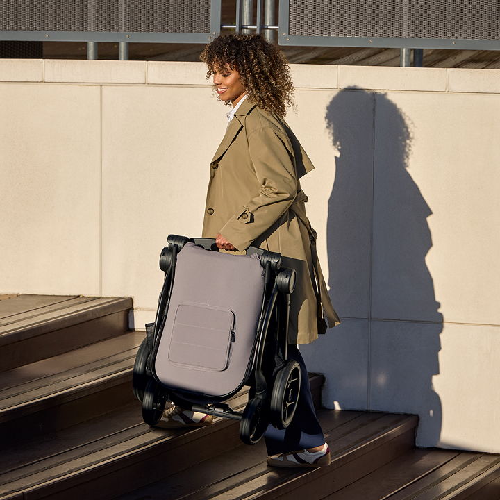 Person carrying a stroller up stairs in bright daylight.