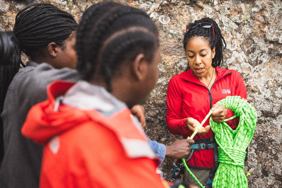 Genevive Walker holds a hank of green Sterling HTP and shows it to two Malawian climbers.