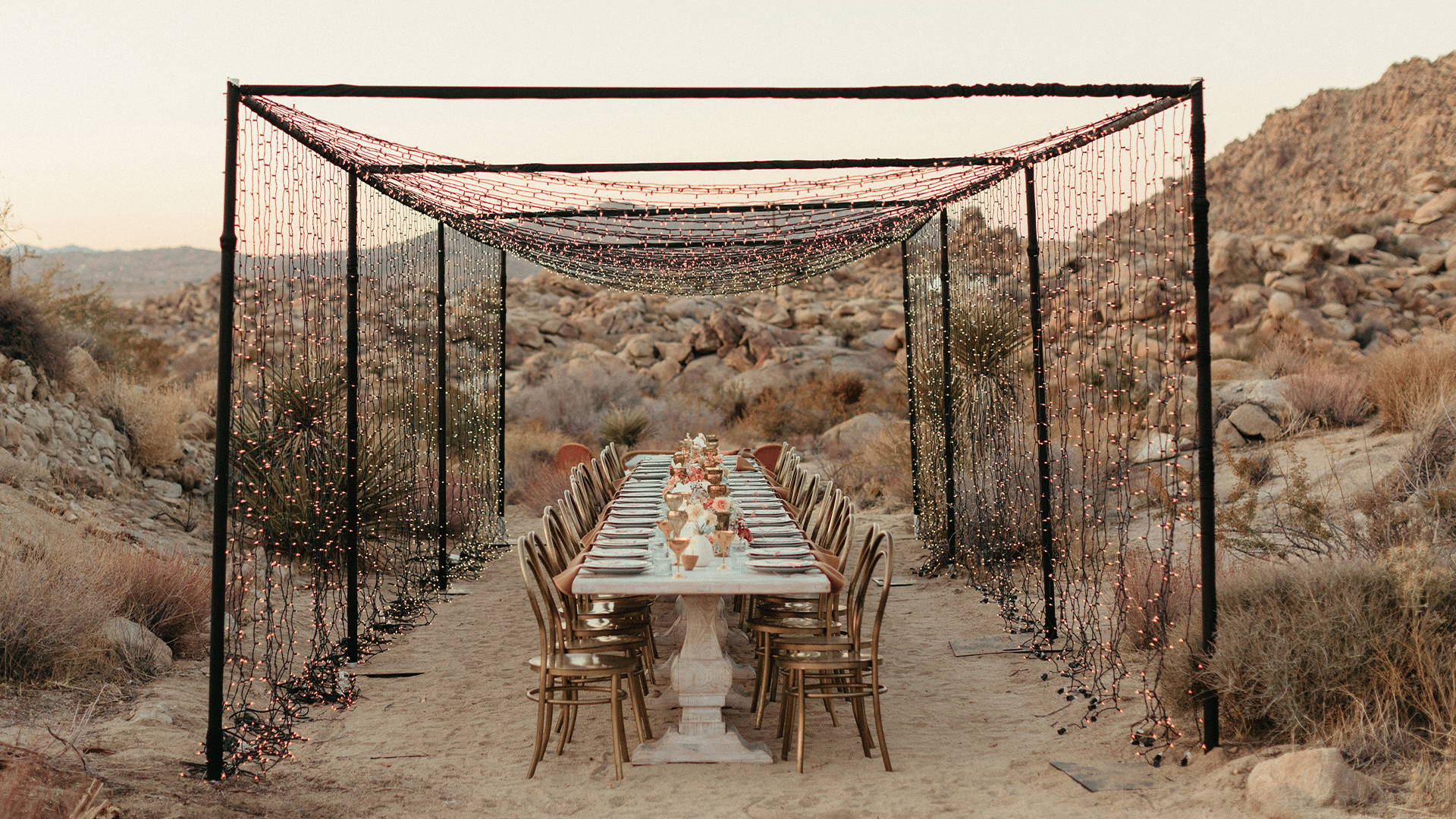 Long wedding table underneath pink fairy lights in desert secenry