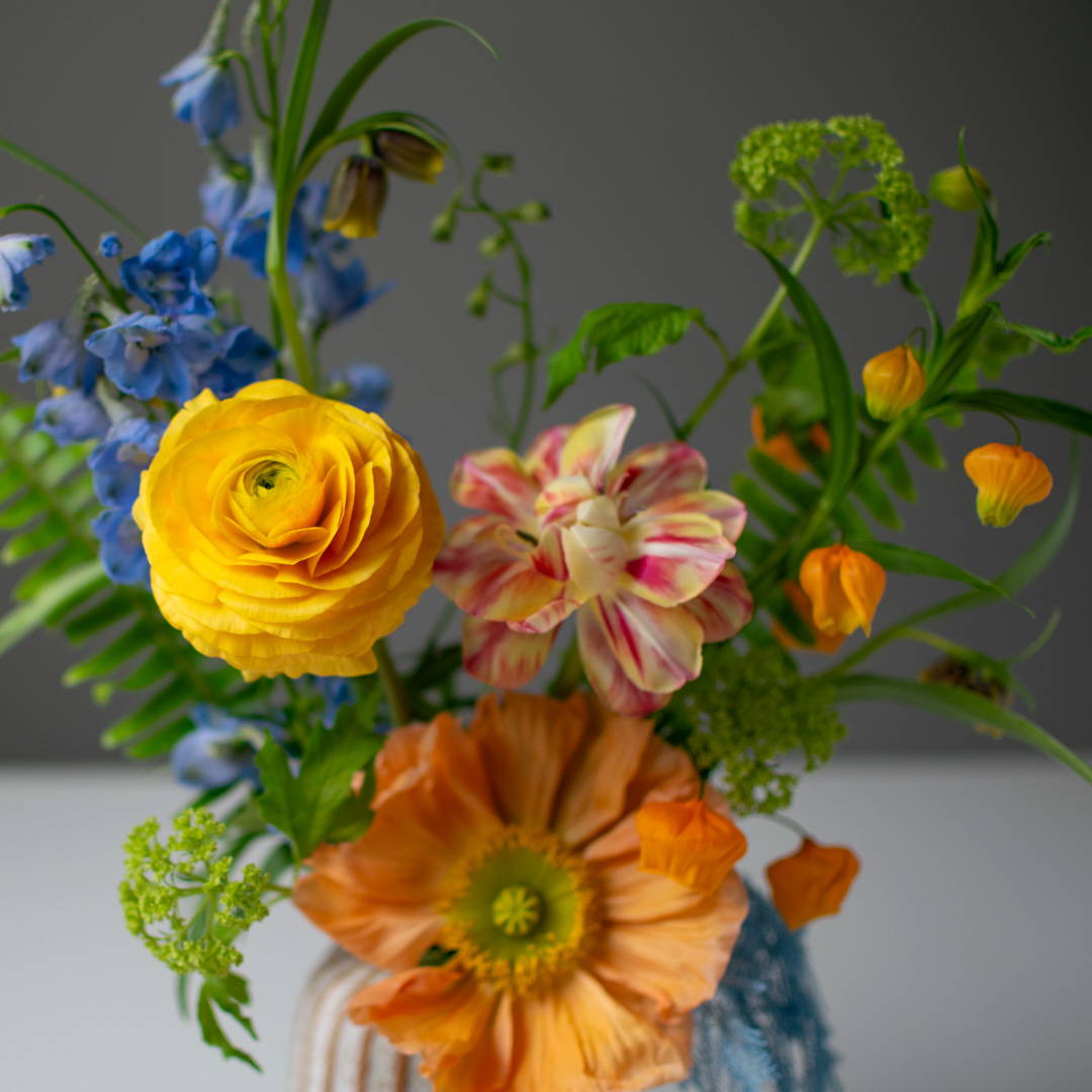 A bright and vibrant spring arrangement with blue, yellow and orange flowers