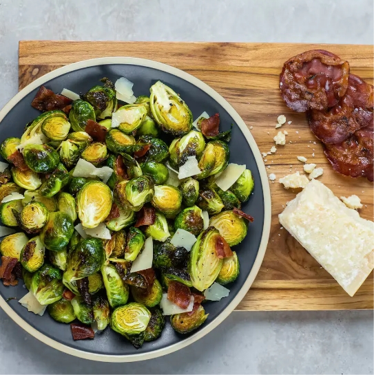 Bowl of sautéed Brussels sprouts with bacon and cheese on a wooden board.