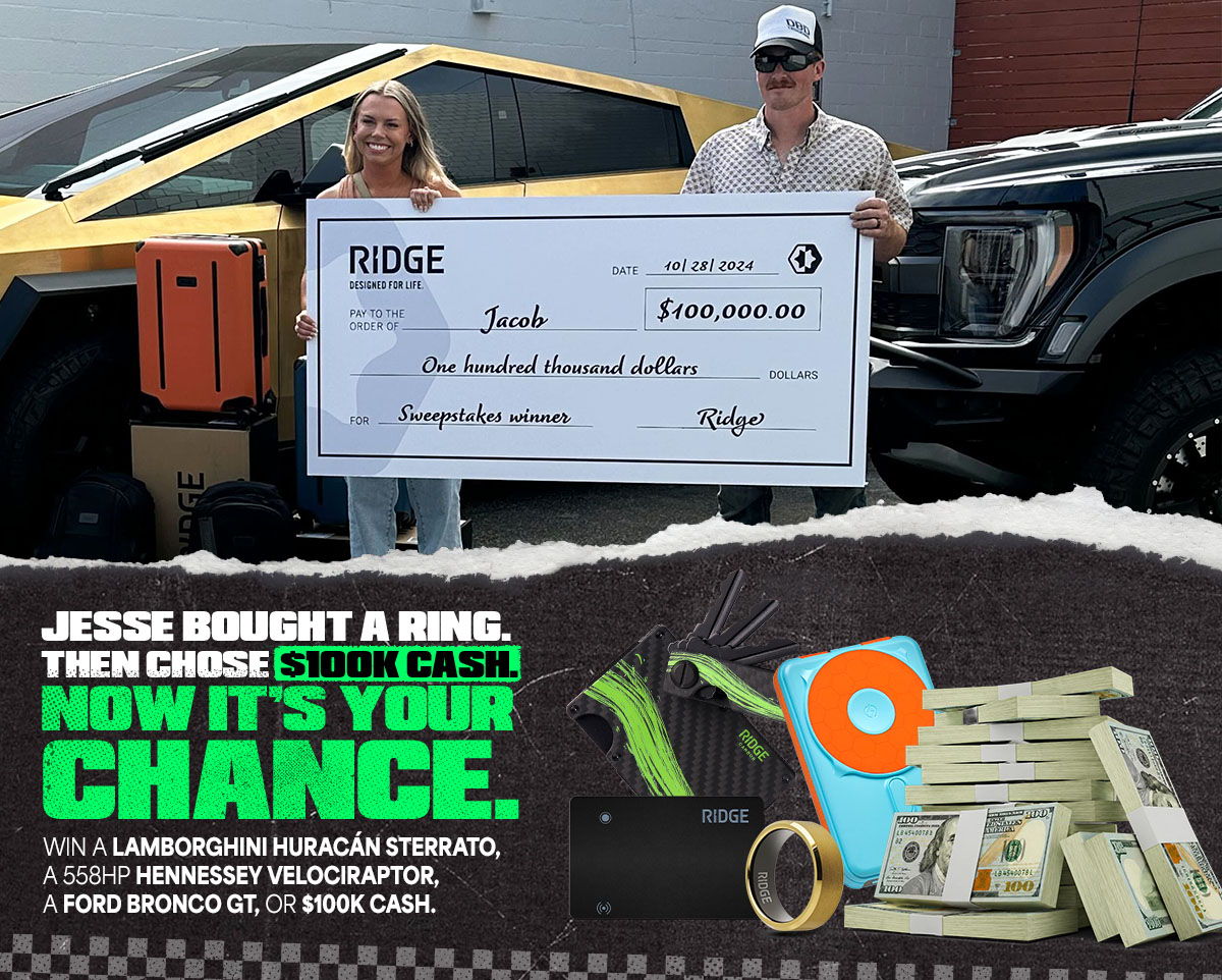 Two people holding a large check with cars in the background.