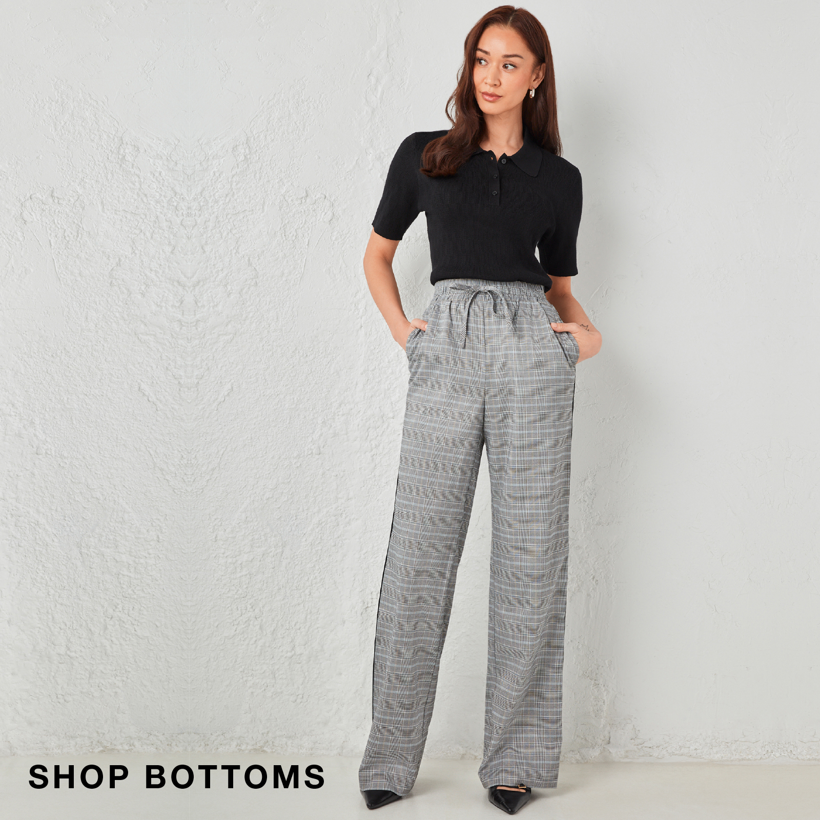 Woman in a black top and gray wide-leg pants standing against a light background.