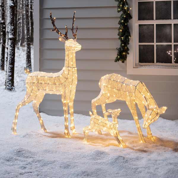 A family of reindeers in an outdoor snowy setting in front of a home
