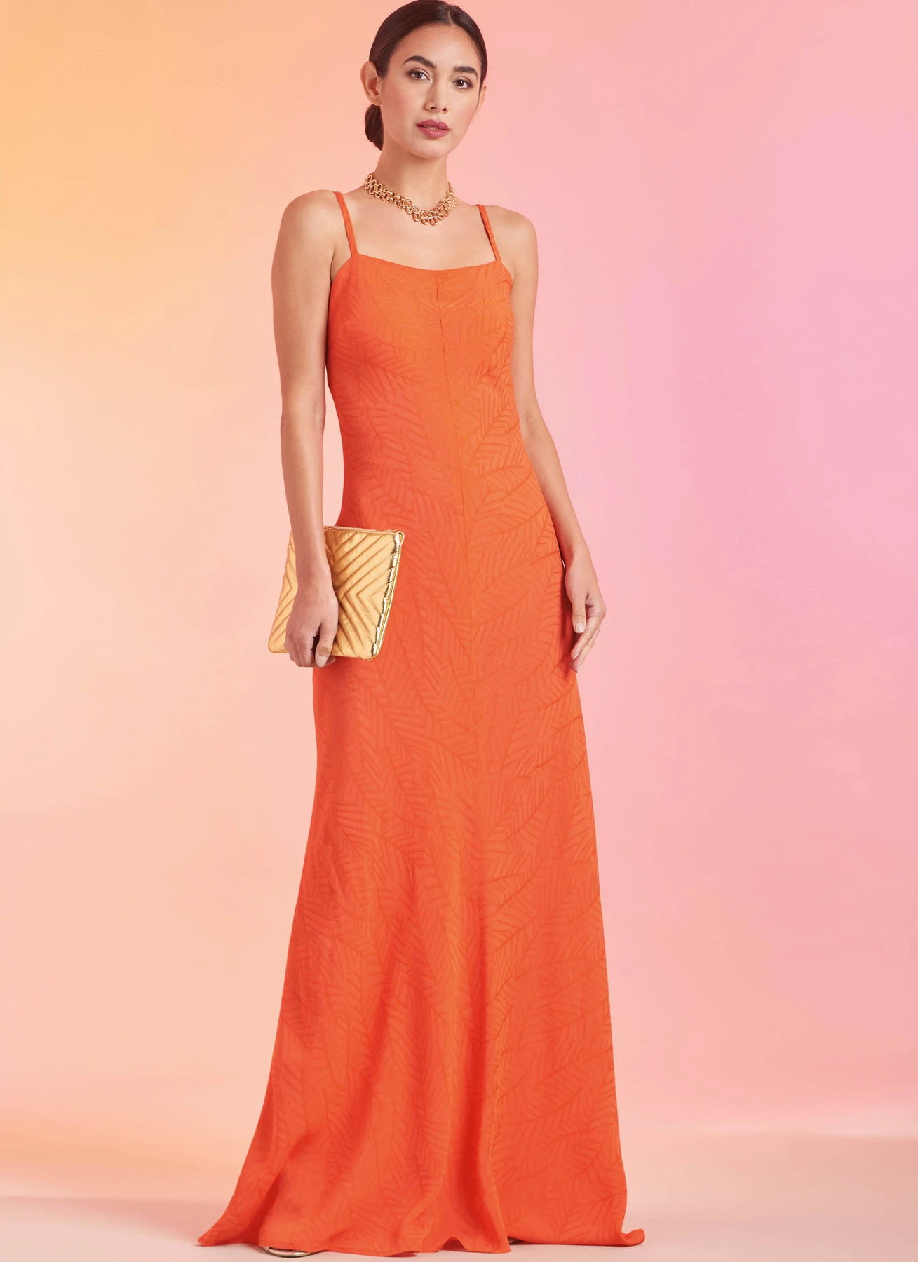 A woman wearing a long orange dress, holding a yellow clutch.
