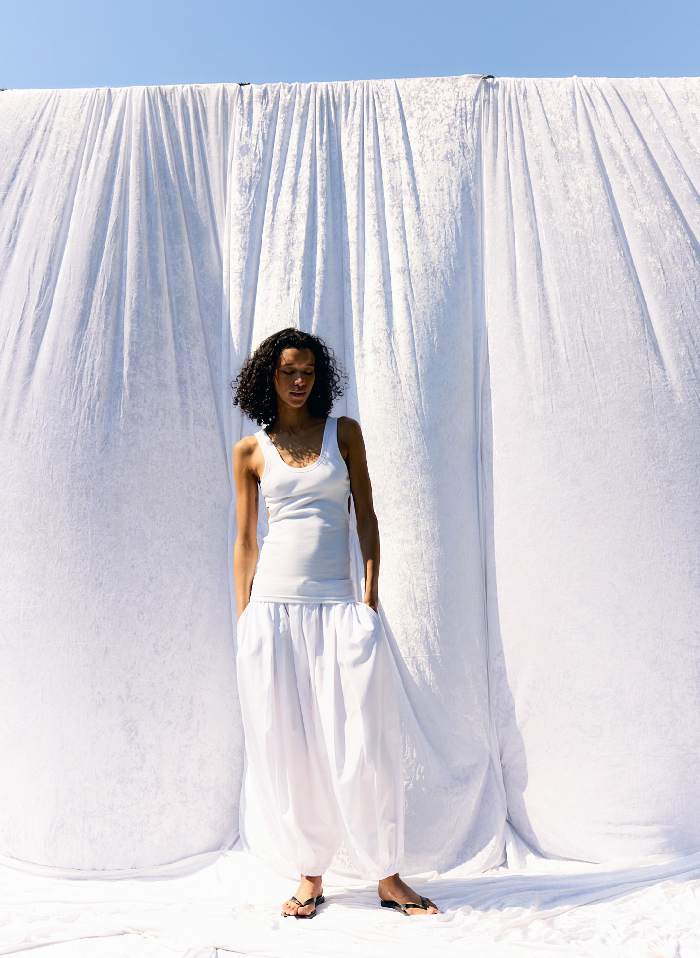 Model in white clothing standing against a white backdrop outdoors.