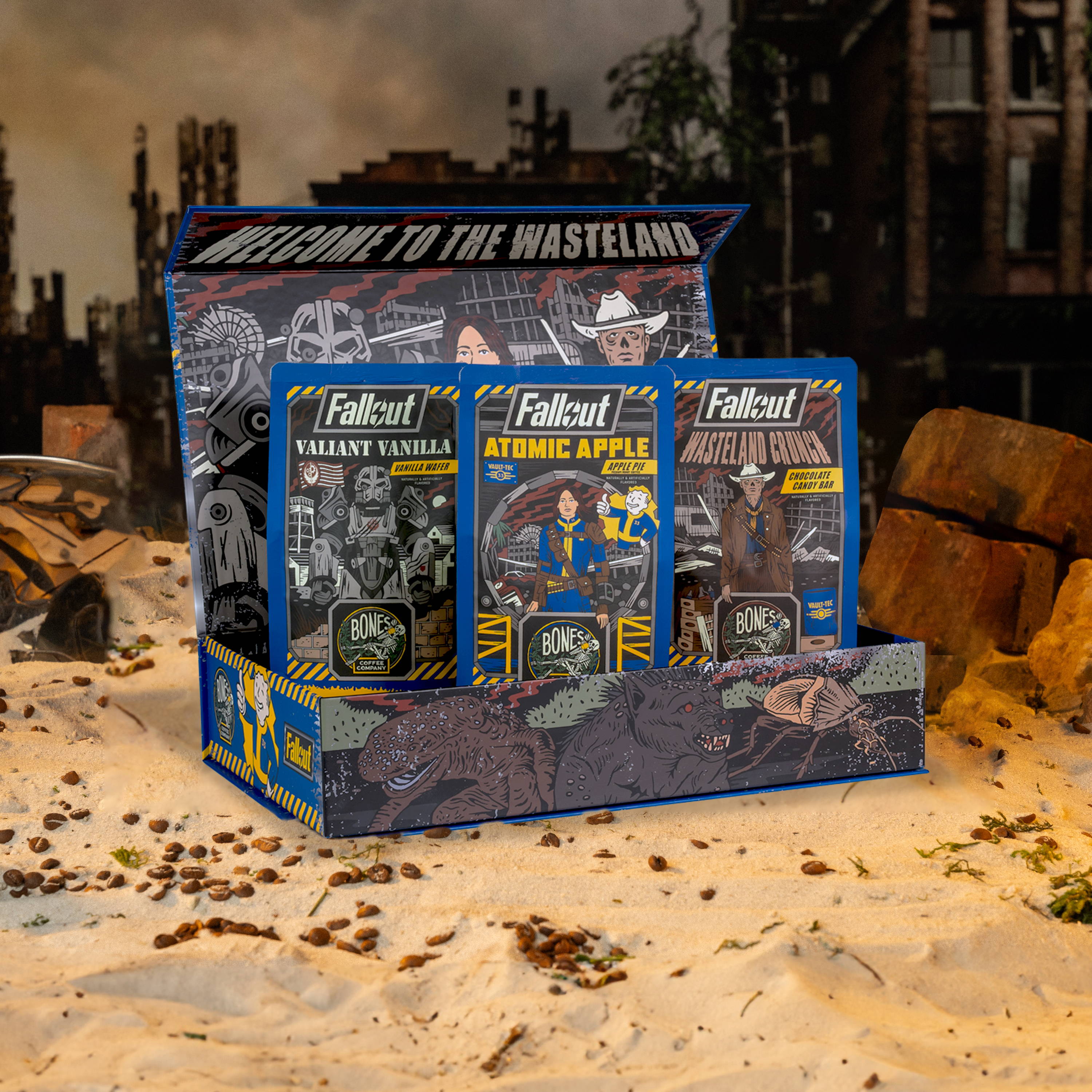 The Fallout Collector's box sits on some sand near broken bricks. Inside the box are three 12 ounce bags of coffee named Valiant Vanilla, Atomic Apple, and Wasteland Crunch.