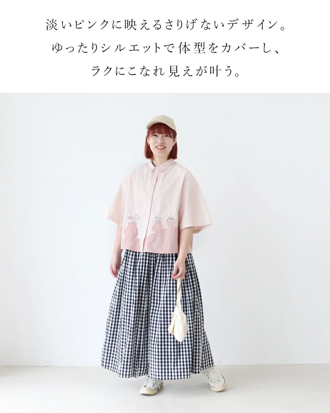 A person wearing a pink top and checkered skirt, posing in a light room.