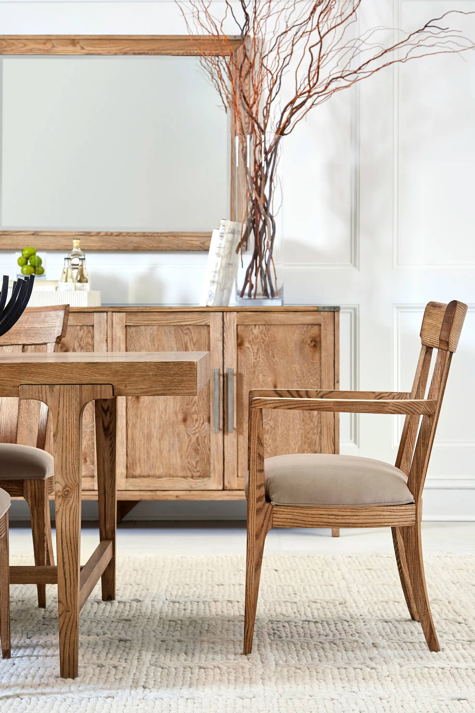 End of wood dining table with wood arm chair, wood cabinet in background