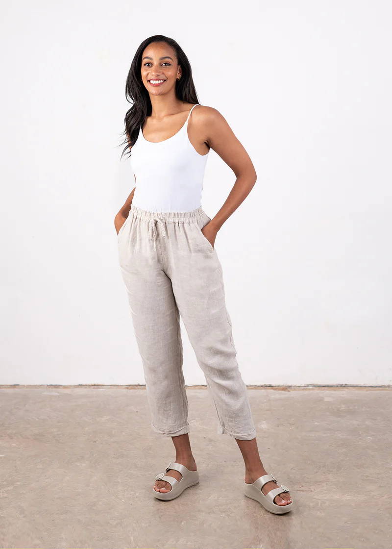 A model wearing a white strappy top, off white tapered linen cropped trousers and off white chunky platform slides