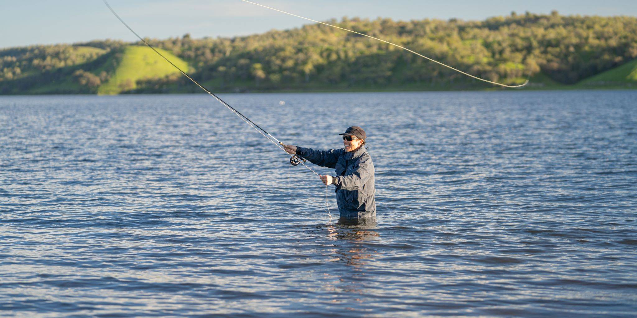 Chris standing in a huge lake casting a fishing line.