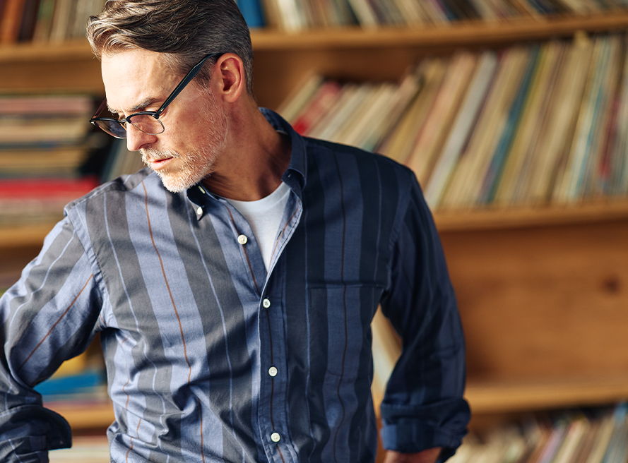 Man in glasses wearing a plaid shirt, standing in front of bookshelves.