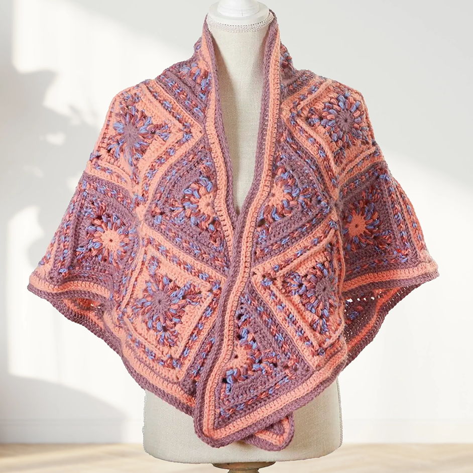 Crocheted shawl in shades of purple and pink displayed on a mannequin.