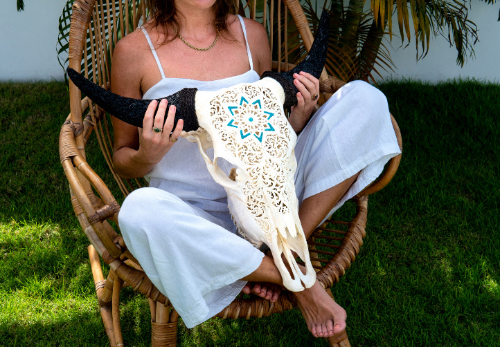 A woman is sitting on a chair in the garden and is holding the carved cow skull Golden Mandala.