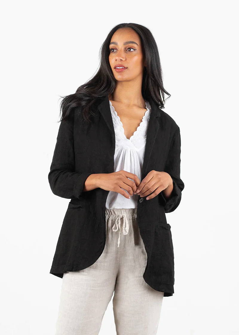 A model wearing a black linen jacket over a white top and off white trousers