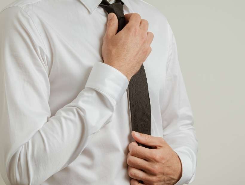 A man wearing a white shirt and adjusting the knot on his black necktie