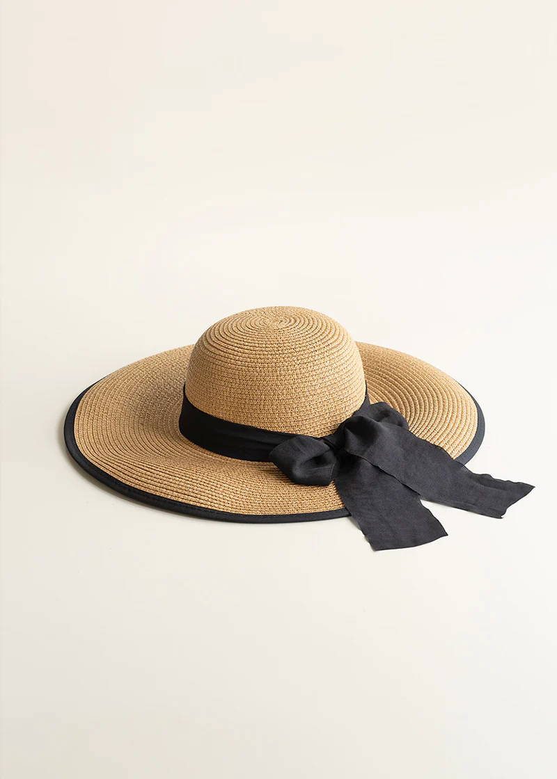 A round brimmed straw hat with ribbon and bow detail and black trim.