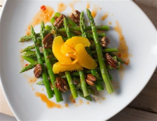 Asparagus salad with orange slices and pecans on a white plate.