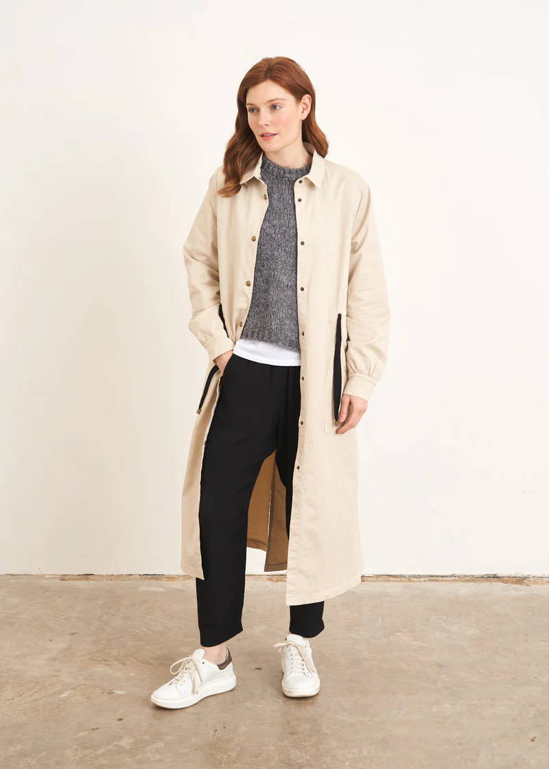 A model wearing a long cream coloured trench coat with a black drawstring waist tie