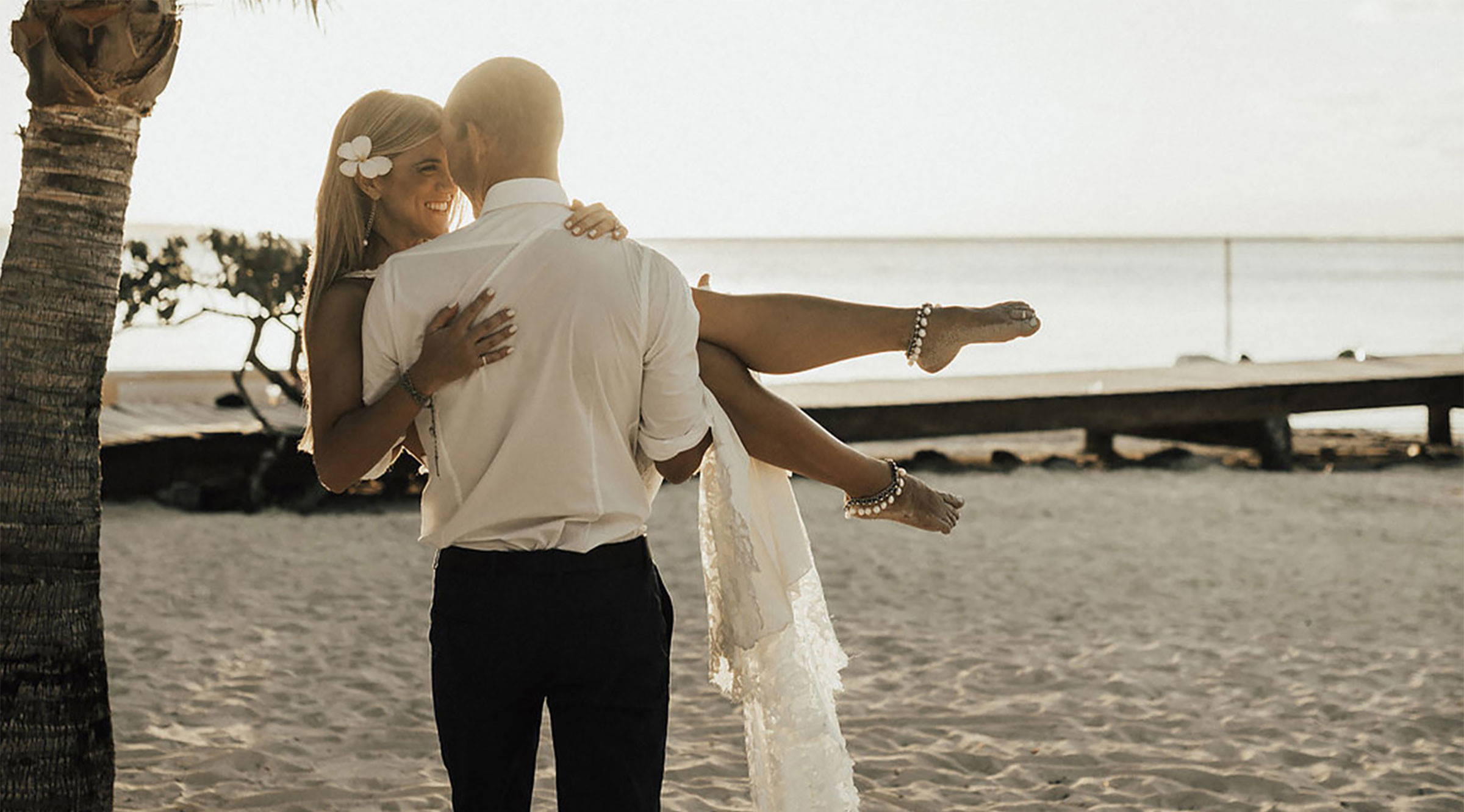 Groom carries bride on beach