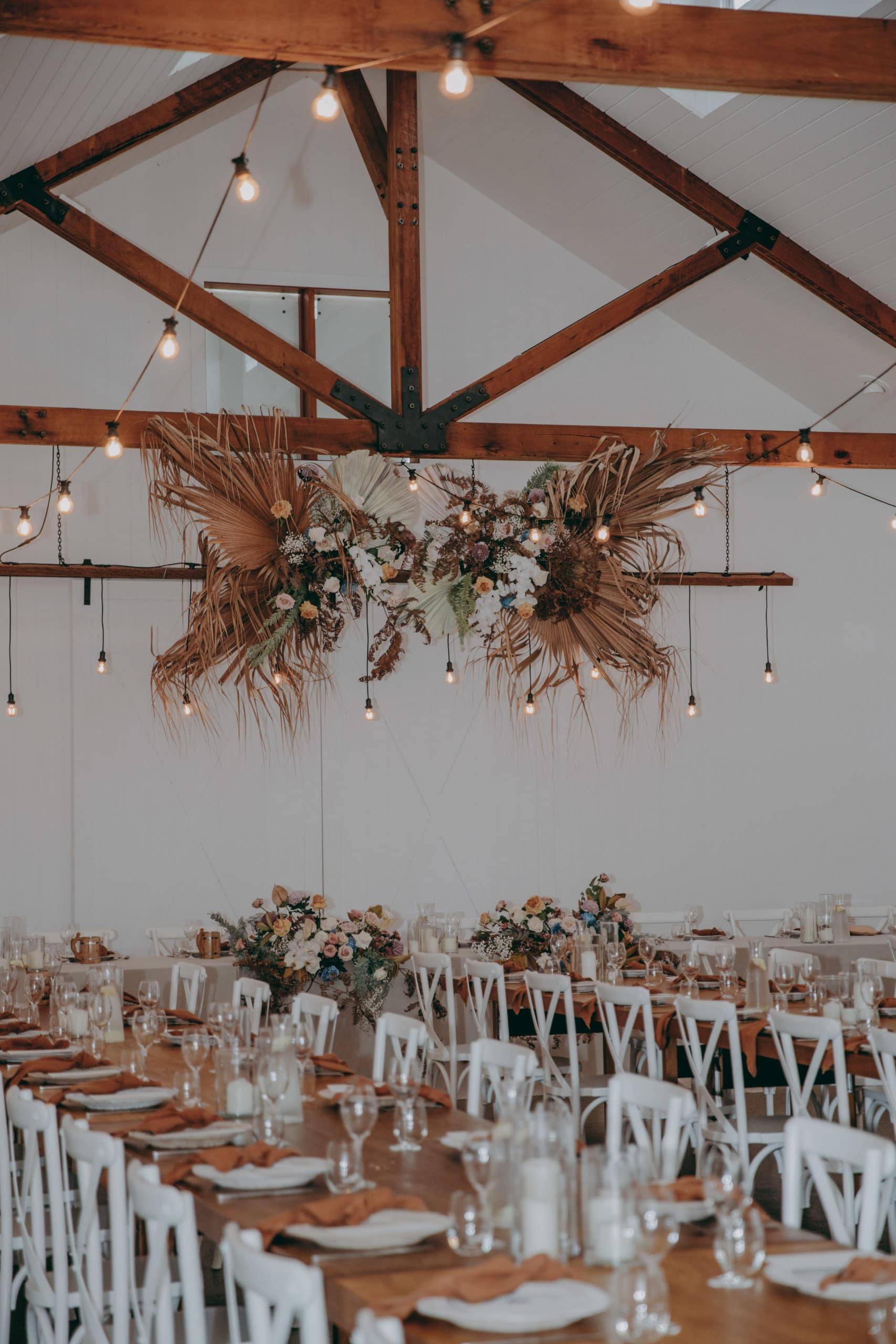 Long tables inside a white barn rustic style with a flower decor and fairy lights 