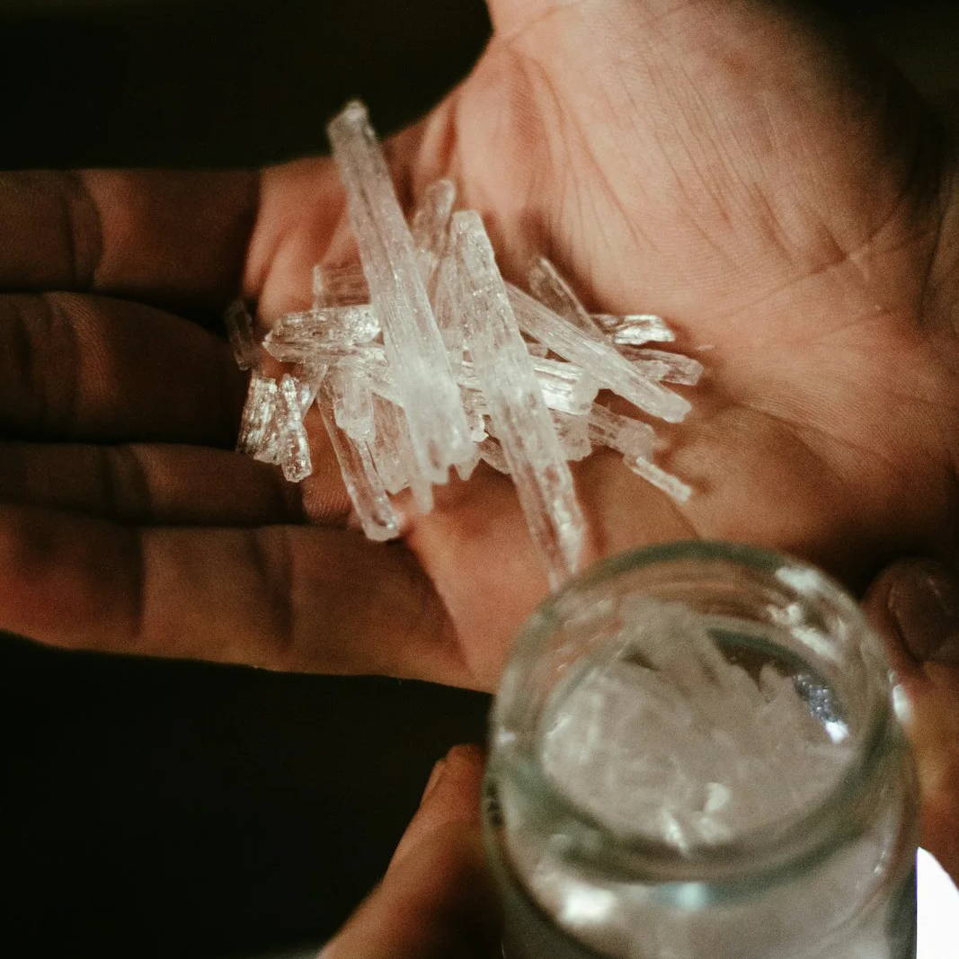 A hand holding menthol crystals above a glass jar.
