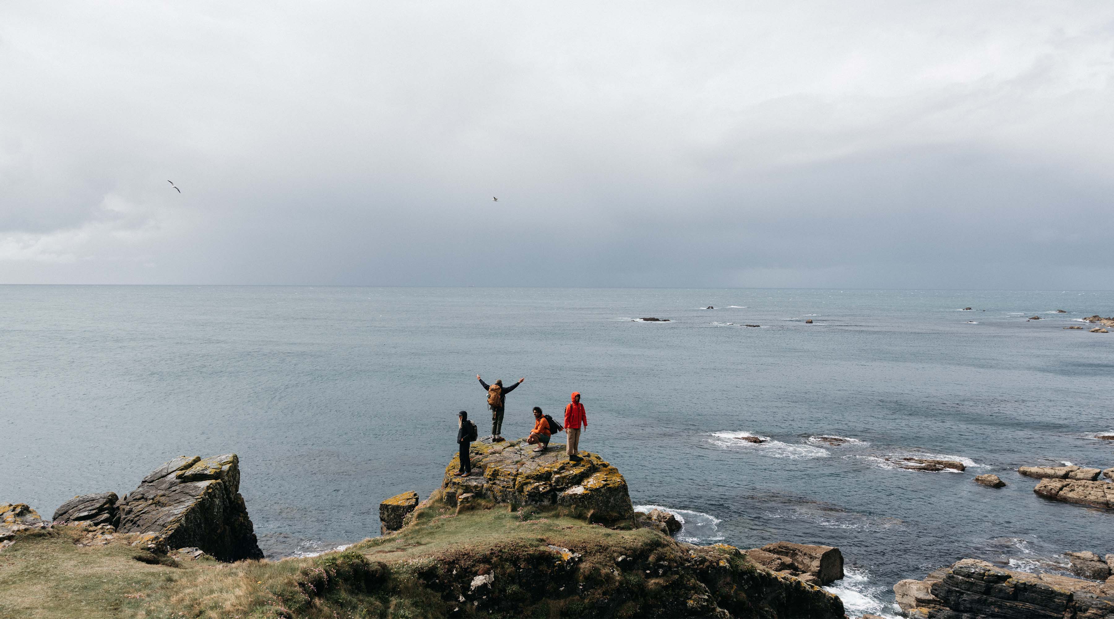 People standing on rocks by the sea under a cloudy sky.