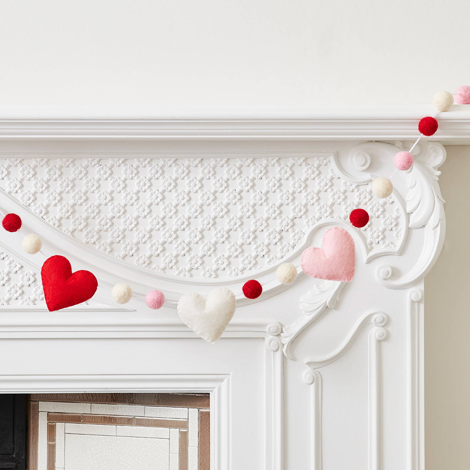 A heart garland with red, pink and cream felt across a white mantlepiece.