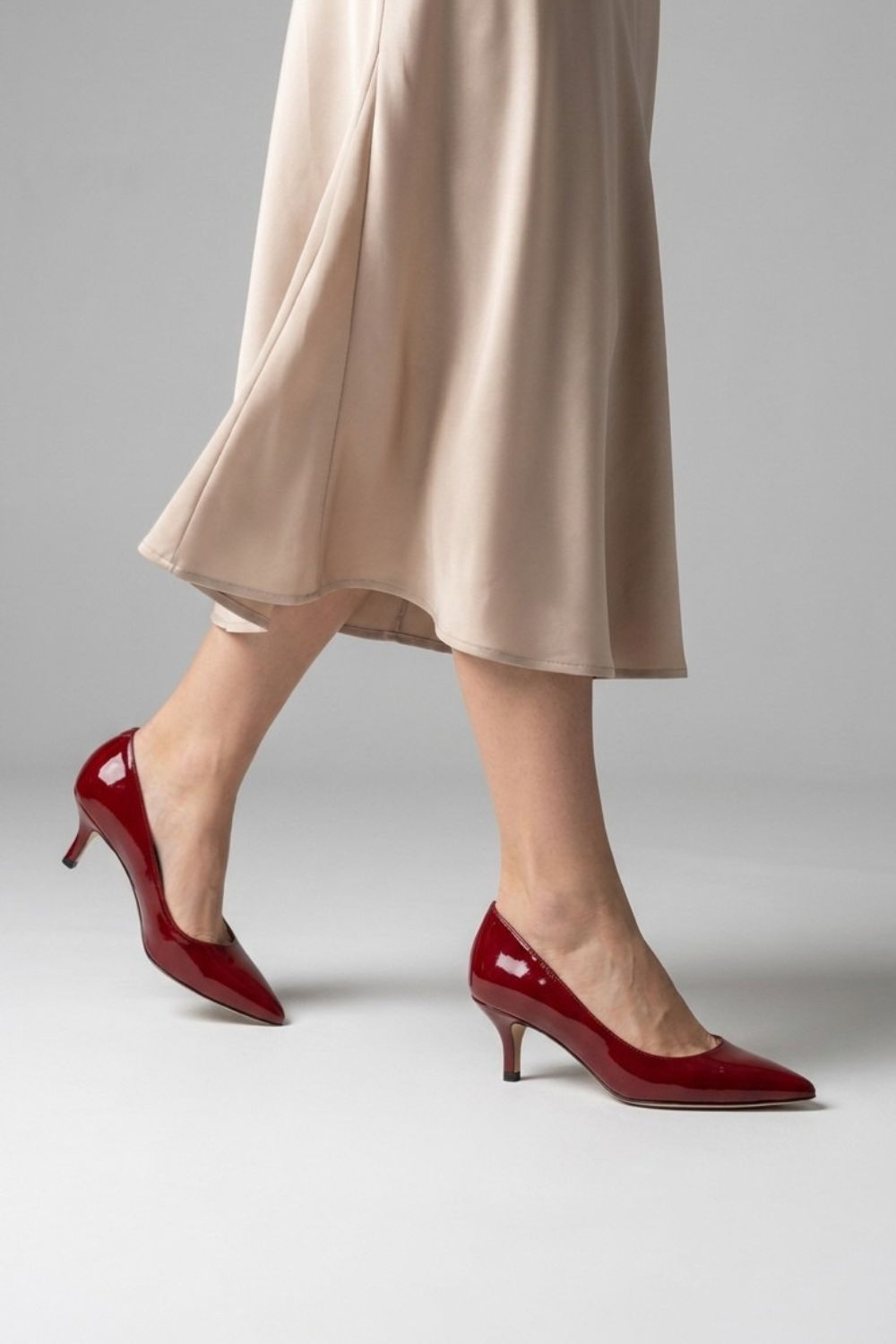 A woman walking in red high heels and a beige dress.