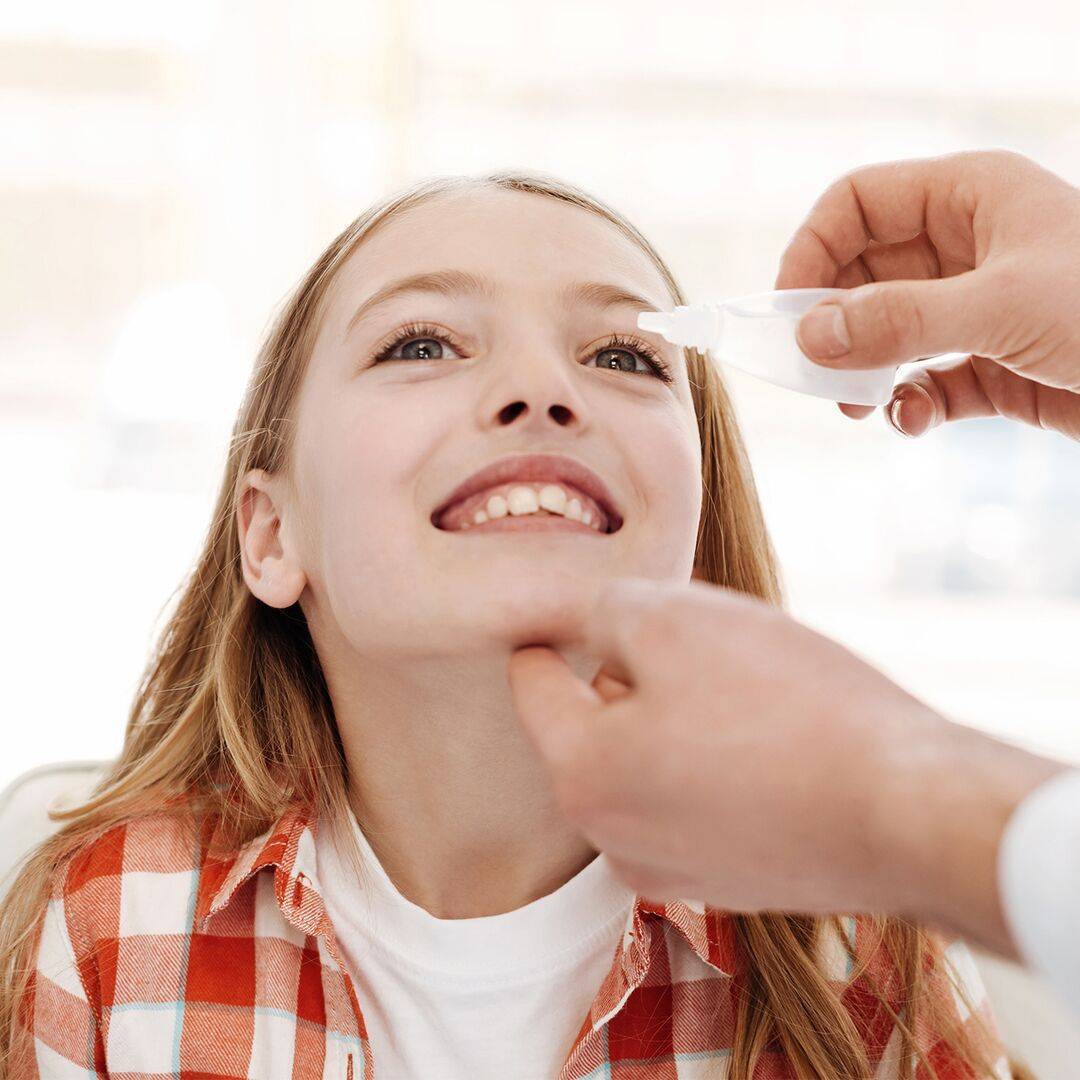 Léky na alergii pro děti existují také v podobě kapek, které dostává i dívka na fotce ke zklidnění podrážděných očí – naklání hlavu dozadu, pro jejich lepší aplikaci 