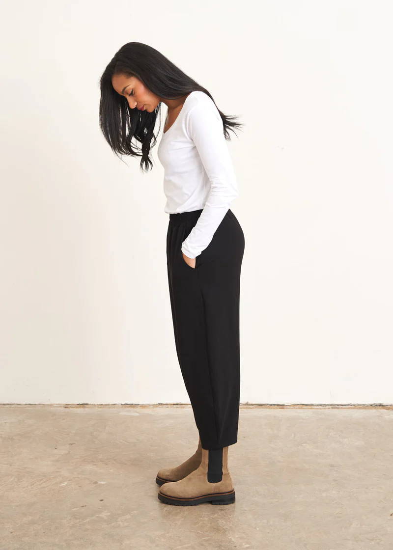 A model wearing a white long sleeved top with black jersey trousers and taupe suede chelsea boots