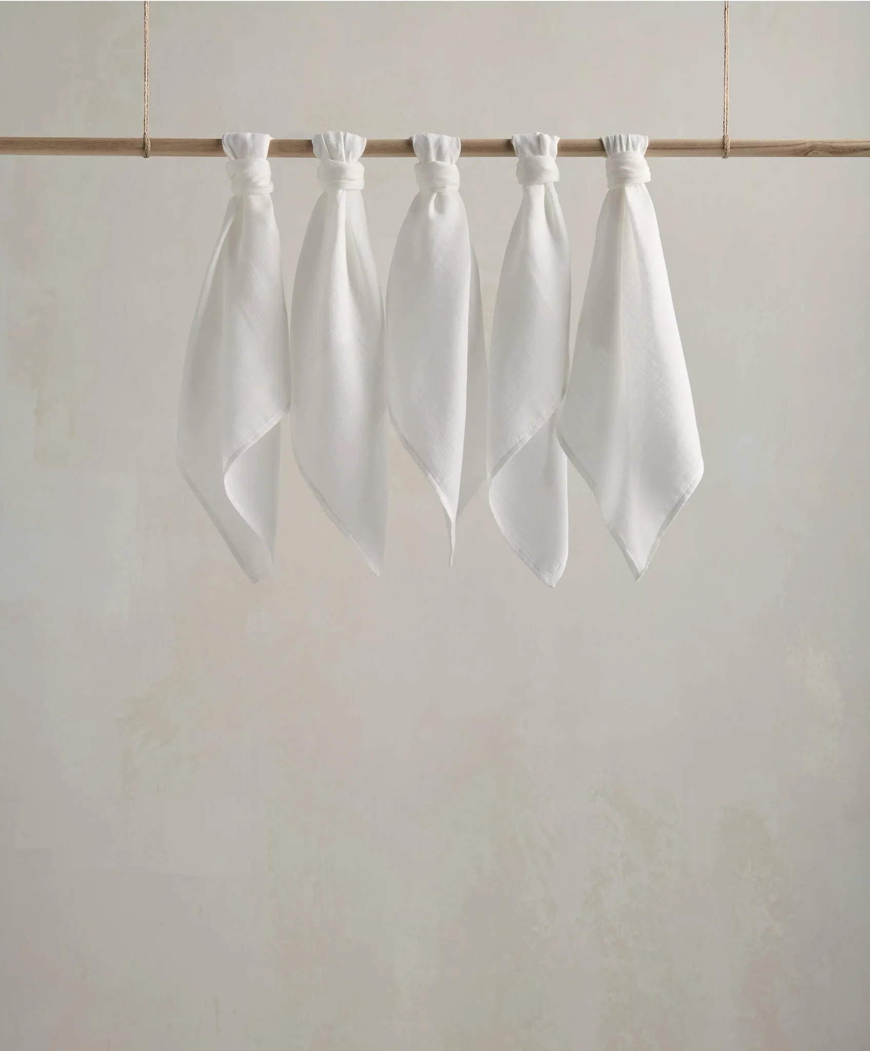 Five white fabric pieces hanging on a wooden rod against a plain background.