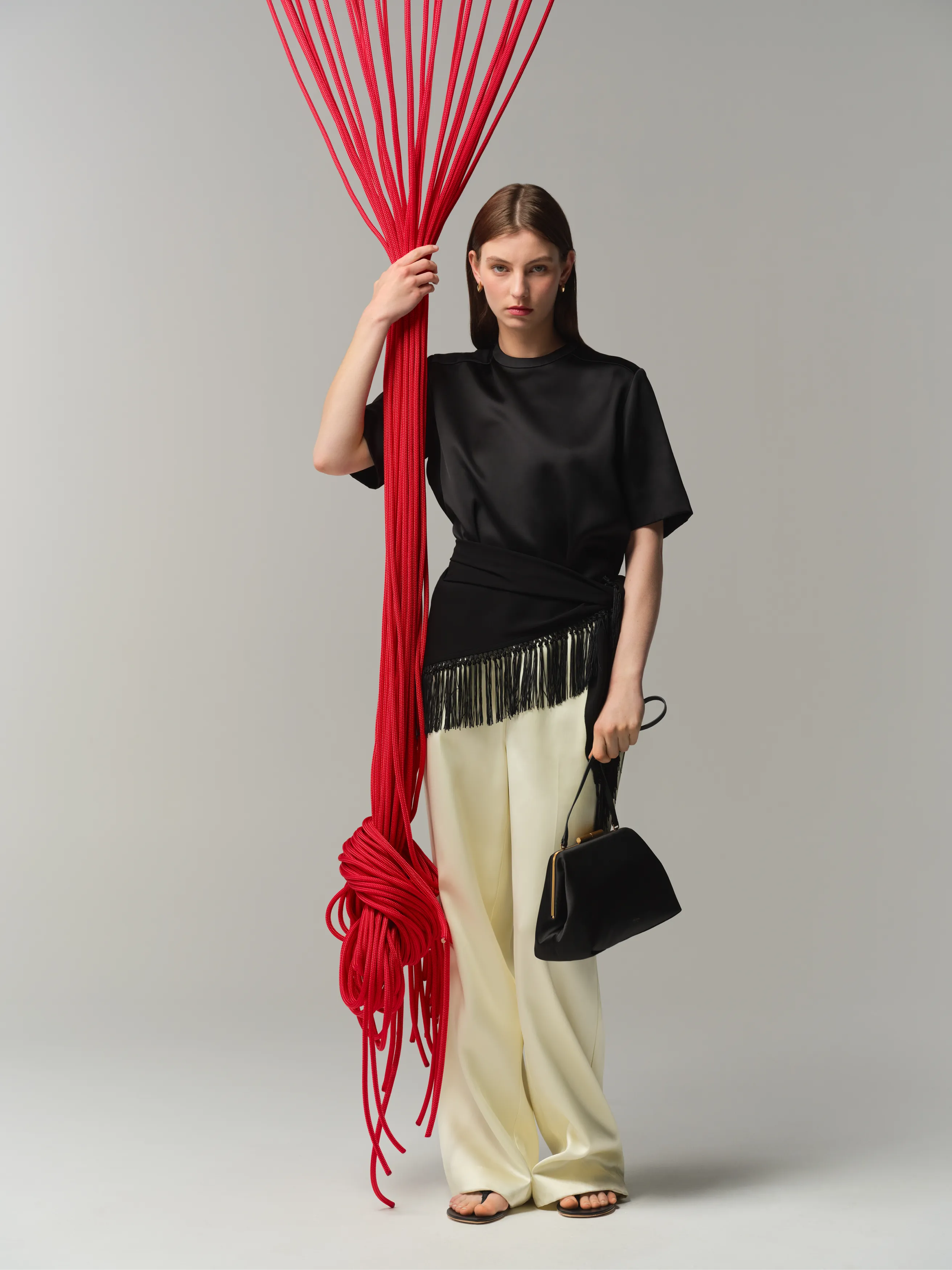 Model in black top and cream trousers holding red strings.