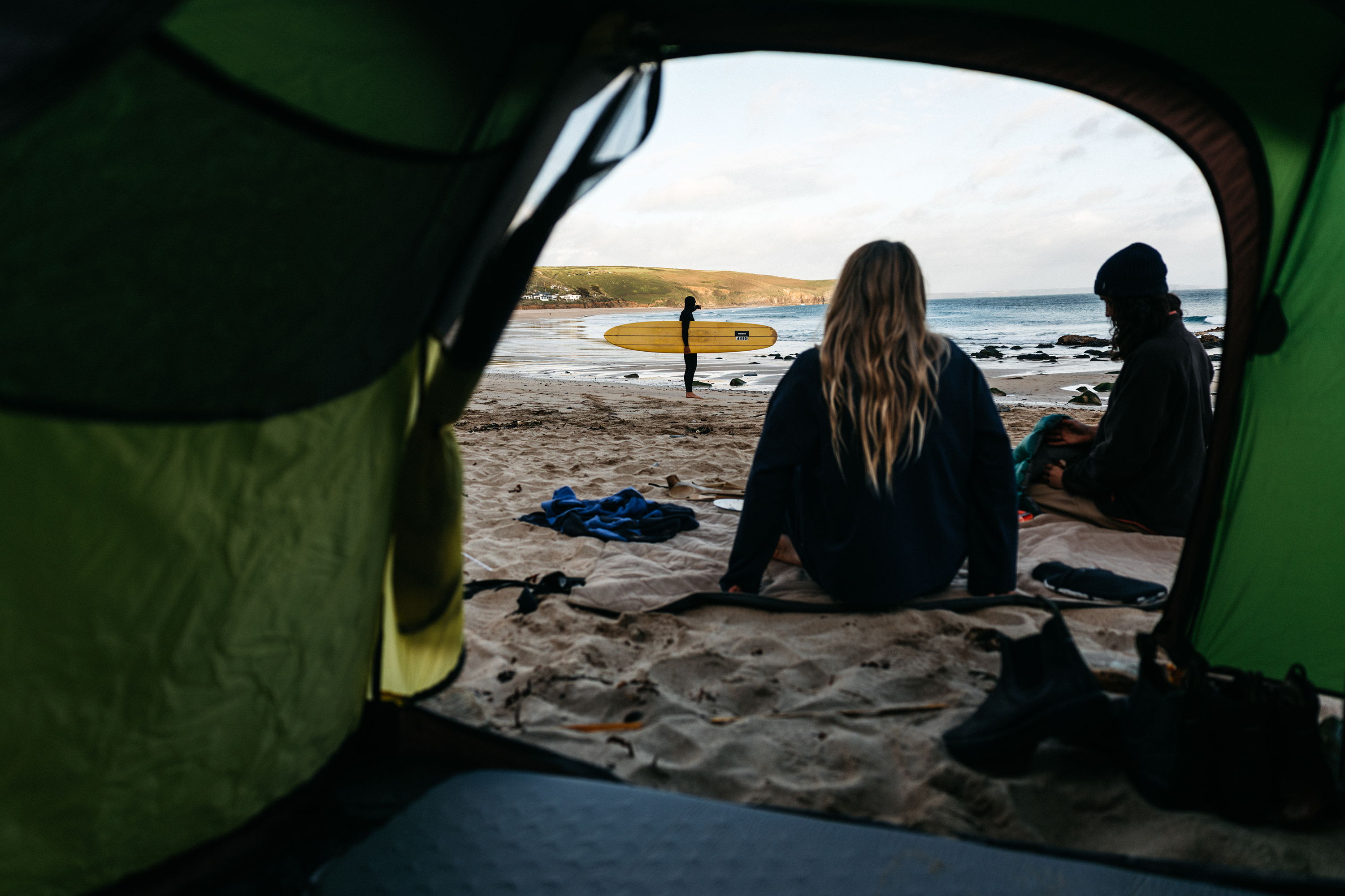 View from a tent of two people by the beach at sunset.