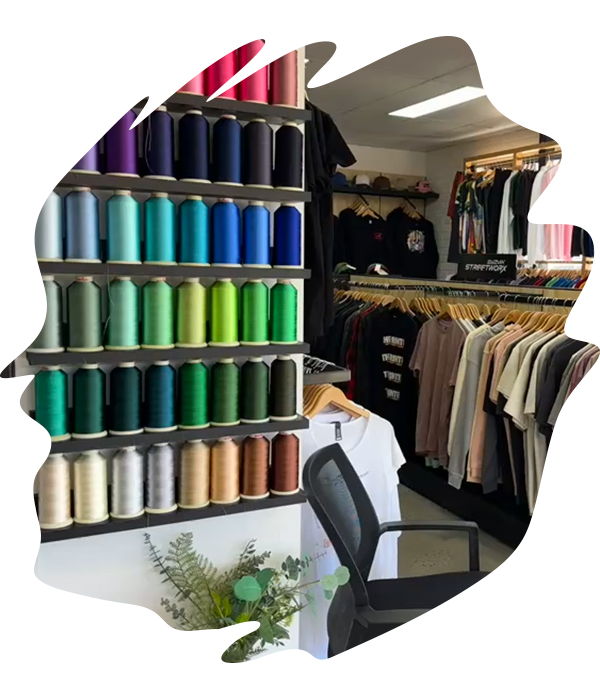 Interior of a print shop showroom showing shelves of colourful embroidery thread spools and garments hanging in the background