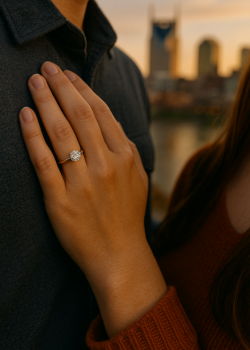 Close-up of a diamond engagement ring on a woman’s hand with city skyline at sunset.