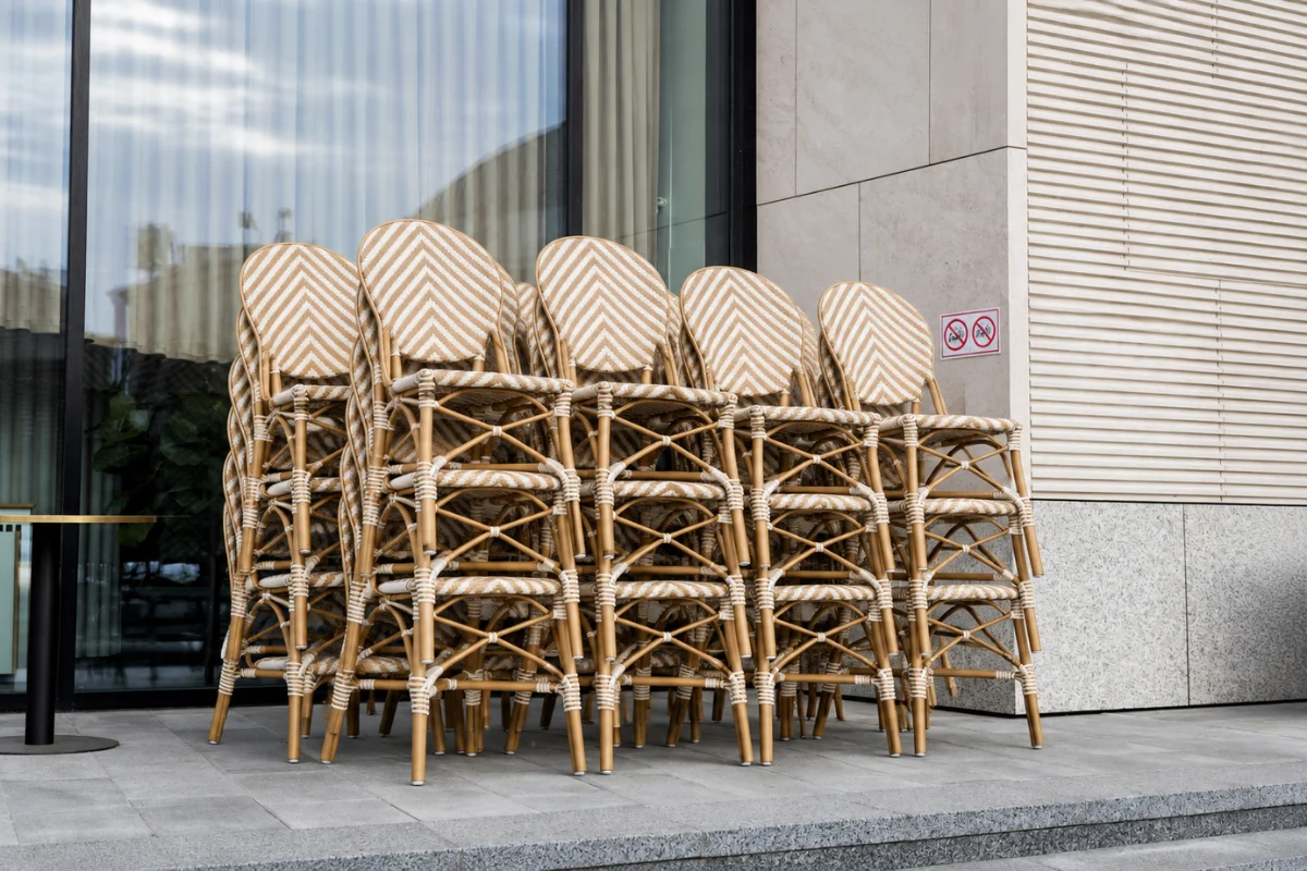 Stacked commercial outdoor rattan dining chairs stored beside a hotel or restaurant patio for replacement stock