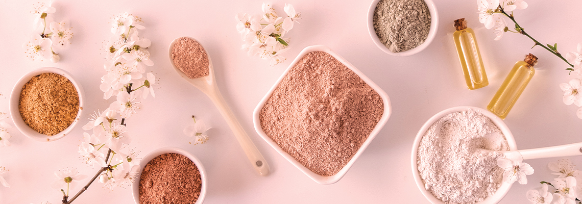 Skincare products and powders arranged on a pink background with flowers.