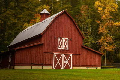A red barn with grass in the foreground and trees in the background