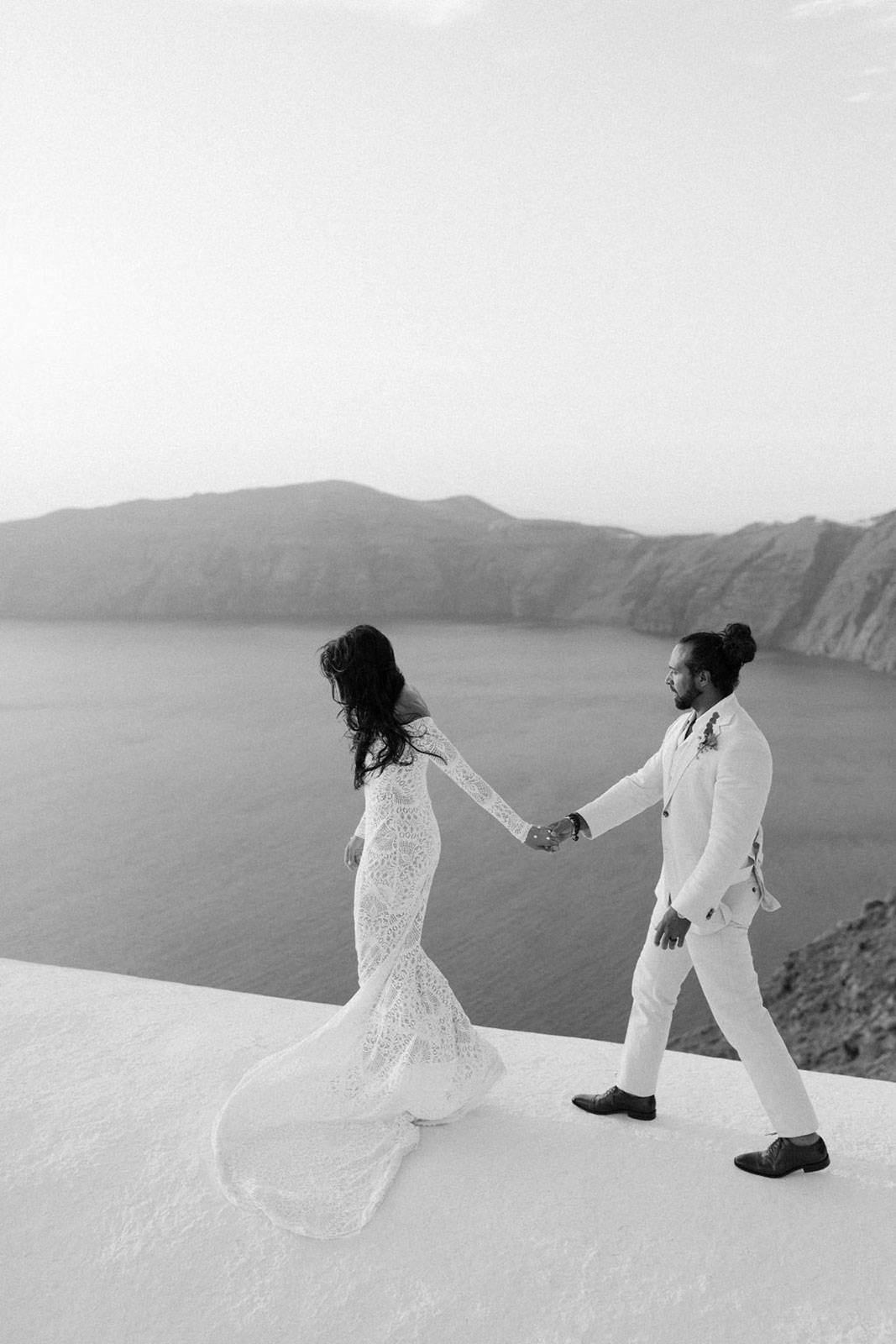 Novios cogidos de la mano con vista al mar de Santorini