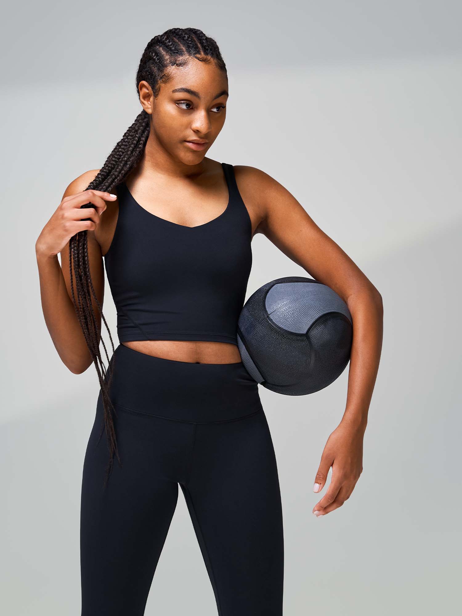 Tall woman wearing a black athletic tanktop and leggings holding a medicine ball