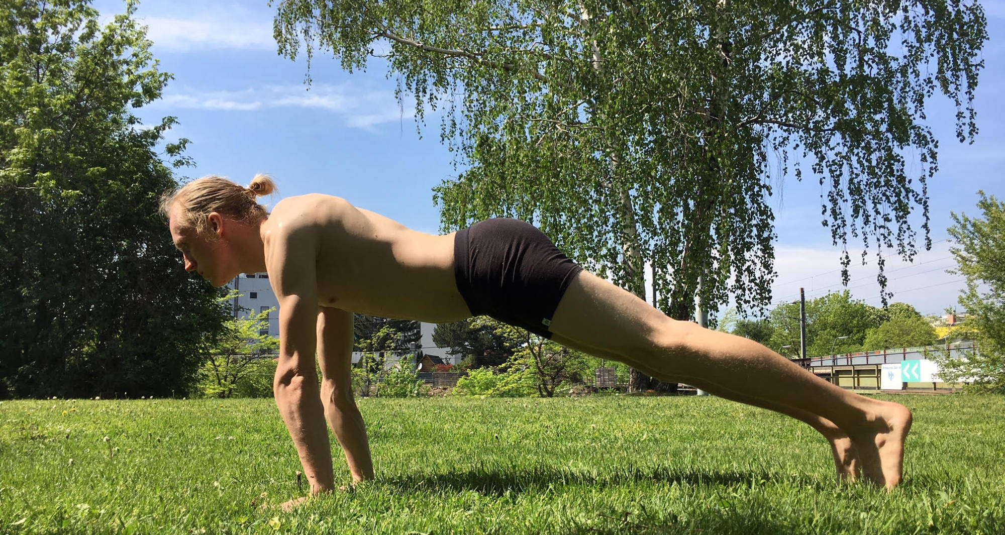 Man planking in a park in a pair of men’s trunks.