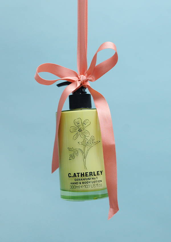 A bottle of hand lotion hanging from a pink ribbon bow.
