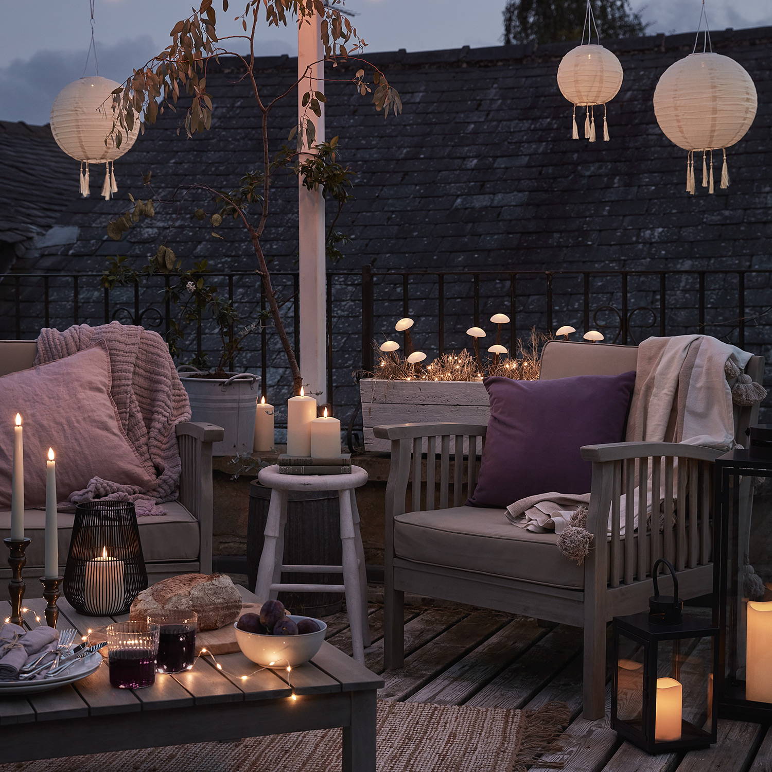 Un coin salon de jardin décoré par des chandelles d'intérieur, des bougies pilliers, des lanternes lumineuses et des lampions suspendus en hauteur. 