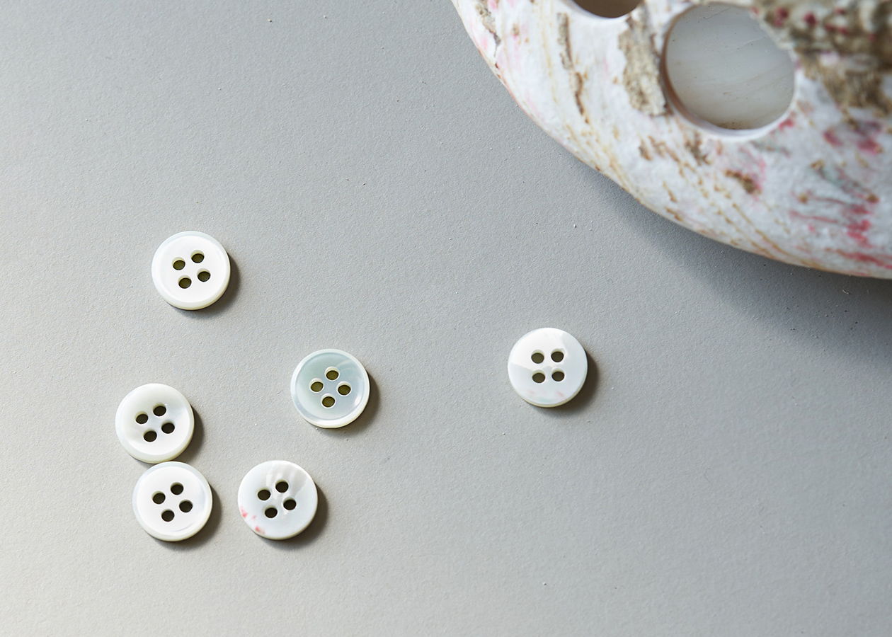 Six white buttons scattered on a gray surface next to a shell.