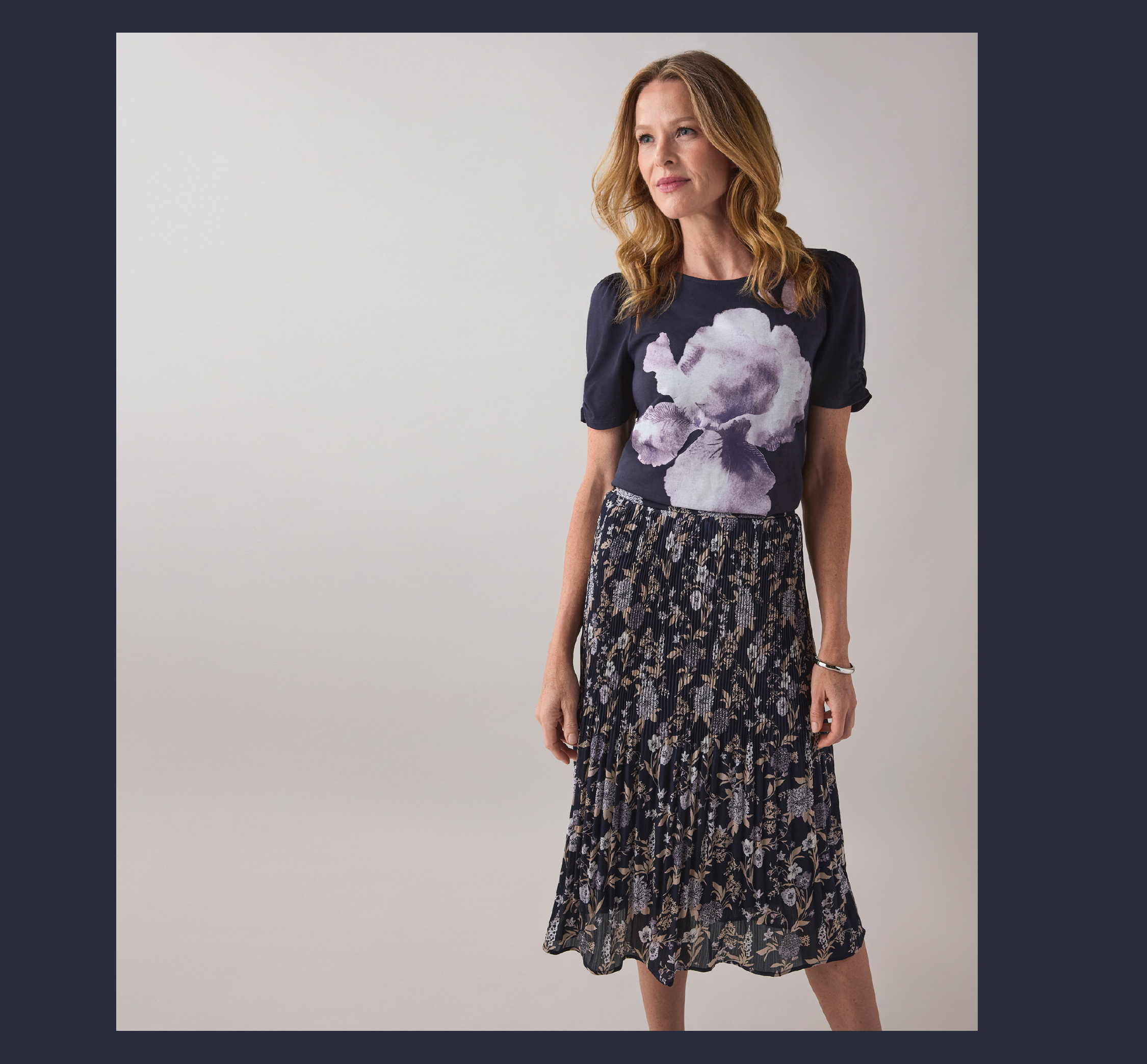 Woman wearing a graphic t-shirt and a floral skirt, standing against a neutral background.