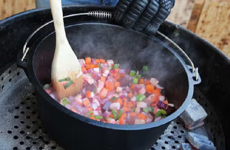 Person stirring colorful vegetables in a pot over a grill.